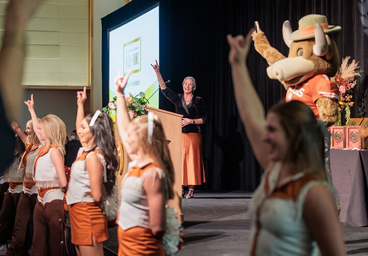 University of Texas cheerleaders giving hook em horns with Bevo and Lillian Mills in background