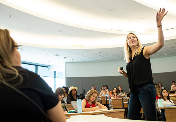 Faculty member gestures while speaking to a full class