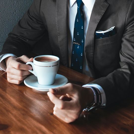 Arms of person wearing a suit and tie holding a cup of coffee