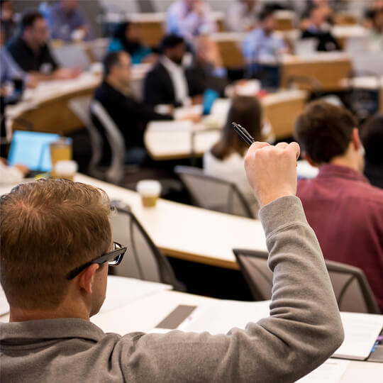 Student in a lecture hall raises their hand