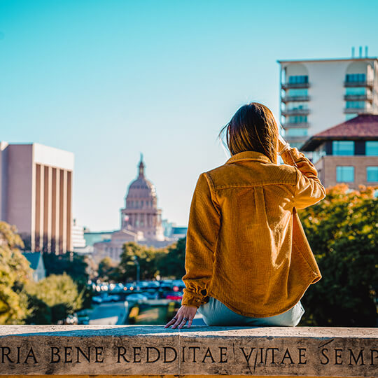 Person sitting on wall looking toward Capitol Building in Austin