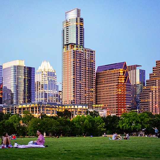 People sitting on grassy field with Austin skyline in background