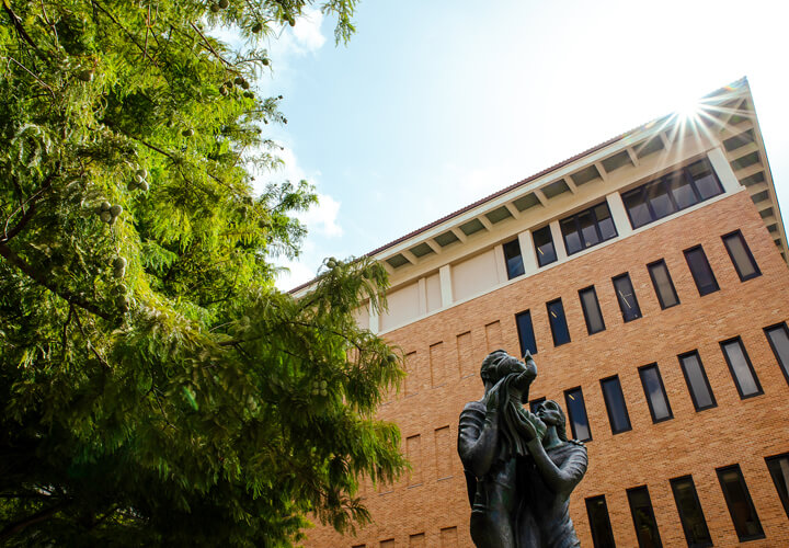 McCombs family statue under a tree against the GSB building