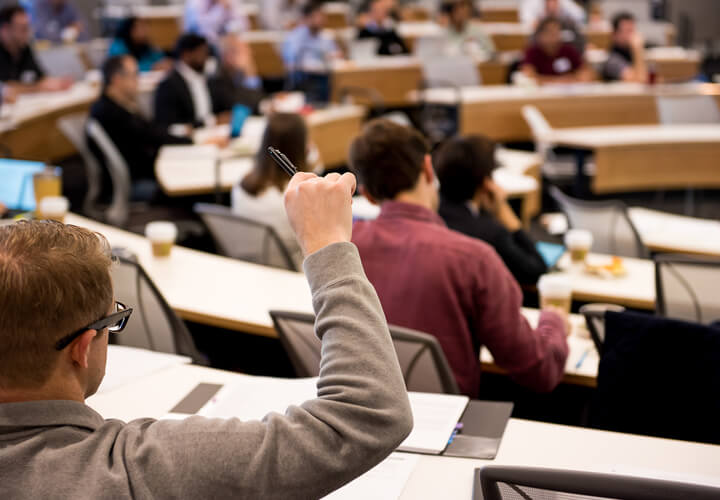 Student in a lecture hall raises their hand