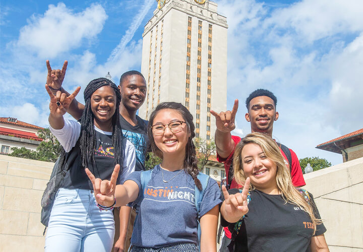 Group of students giving hook em horns with University of Texas tower in the background