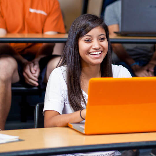 Smiling student sitting in a classroom with a orange laptop