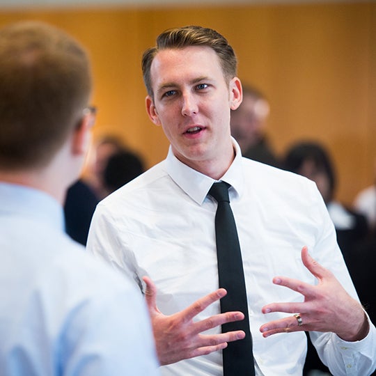 Student with shirt and tie gesturing while in a conversation