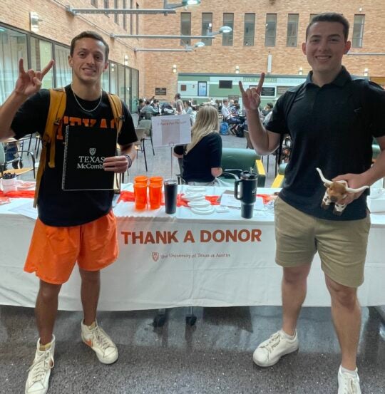 Two students at an event showing Hook 'Em Horns