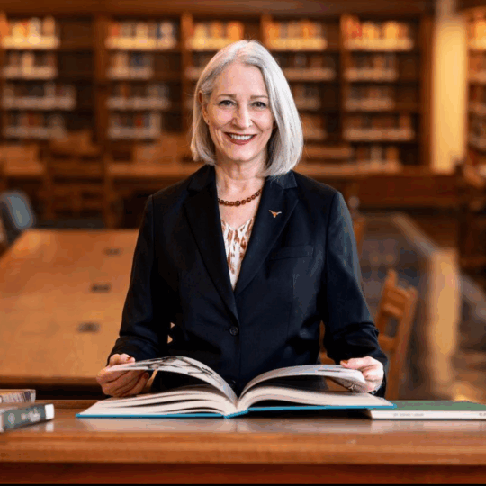 Dean Lillian Mills smiling with an open book in the library