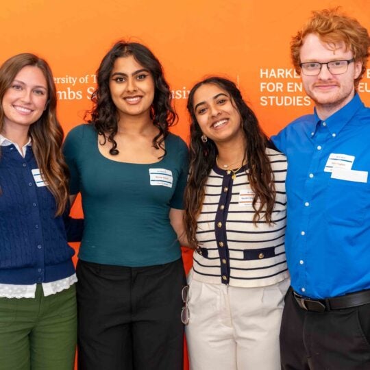 Group of students posing in front of an orange backdrop