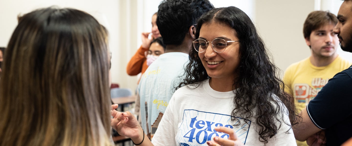 Focus on student wearing glasses in a group of students mingling in class